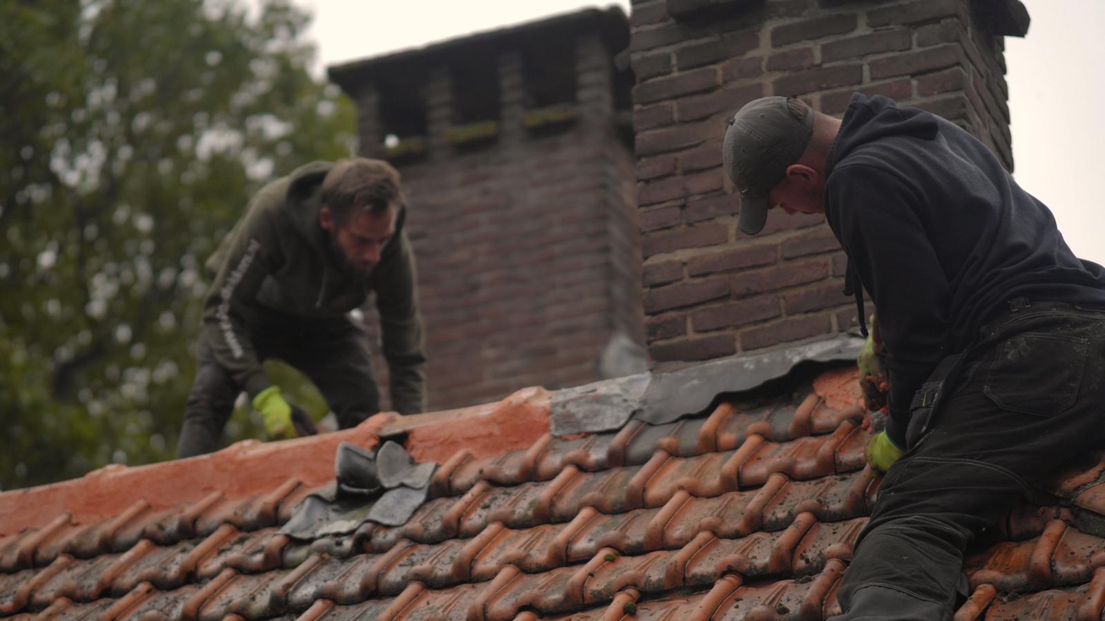 Twee dakdekkers werken aan de nok en het loodwerk van een pannendak