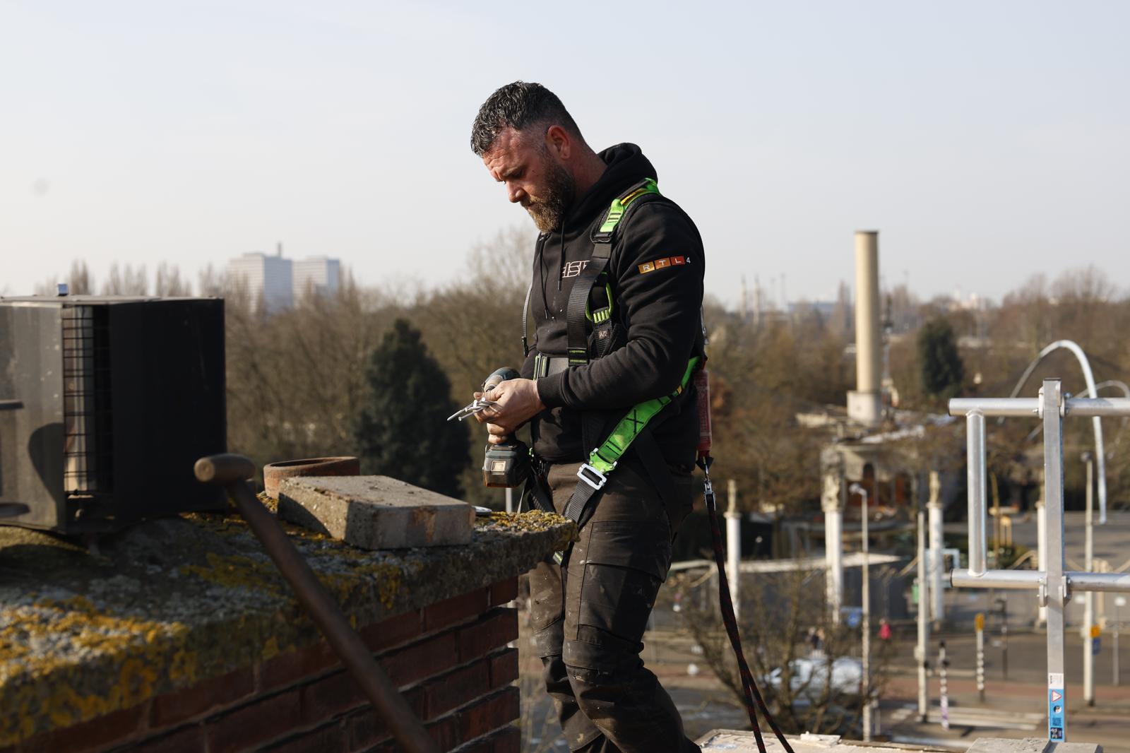 Dakspecialist werkt op plat dak met veiligheidsharnas
